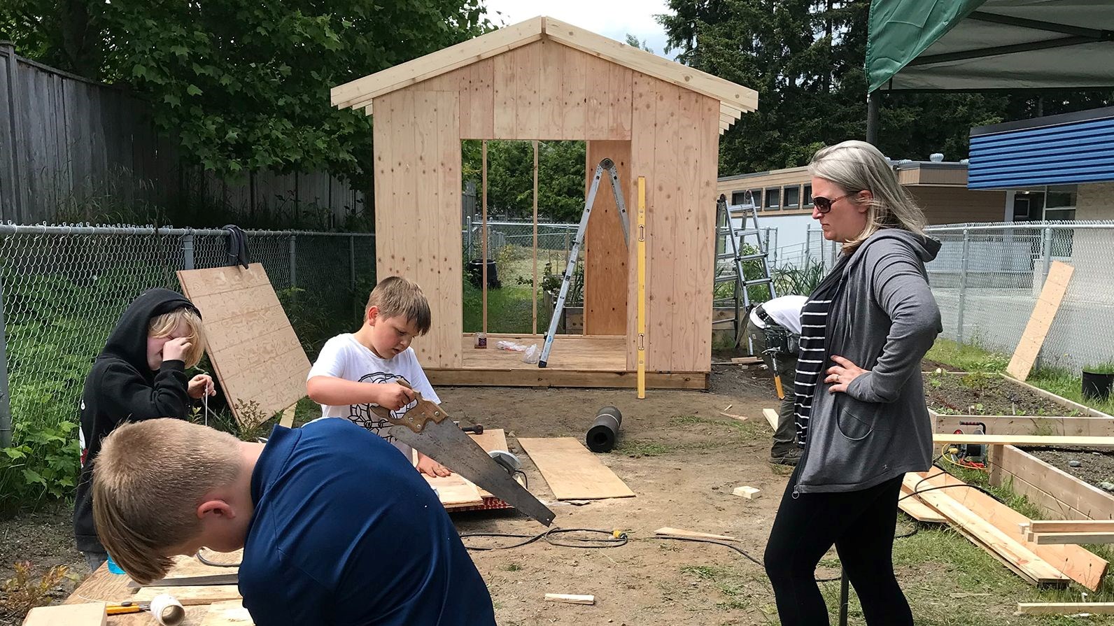 Teacher watches as students help with sawing wood for the shed.